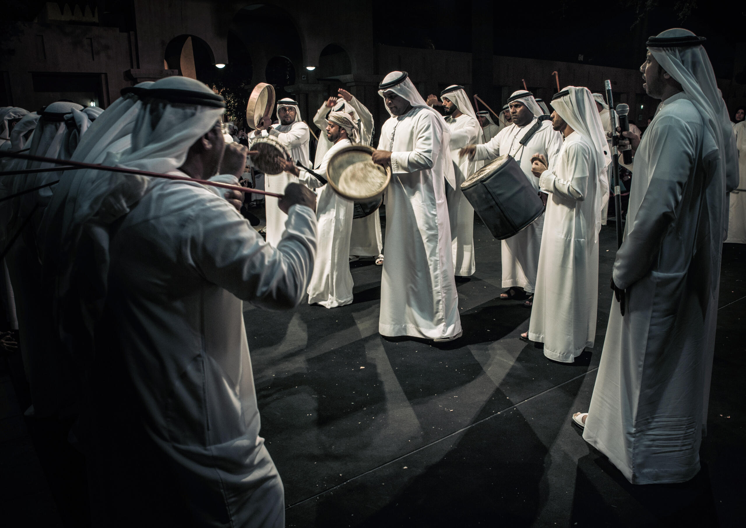 A group of Emirati men dressed in traditional kanduras perform the Al Ayyala dance, a UNESCO-recognized cultural heritage of the United Arab Emirates. This traditional performance, featuring synchronized movements and rhythmic drumming, reflects the values of unity, hospitality, and national identity deeply rooted in Emirati culture.