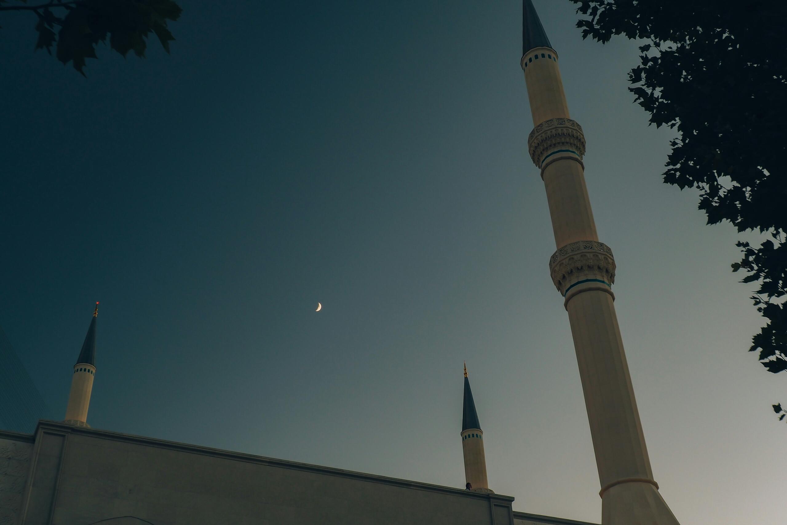 Mosque minarets under a crescent moon at dusk the Islamic lunar calendar determines the Islamic New Year holiday in the UAE