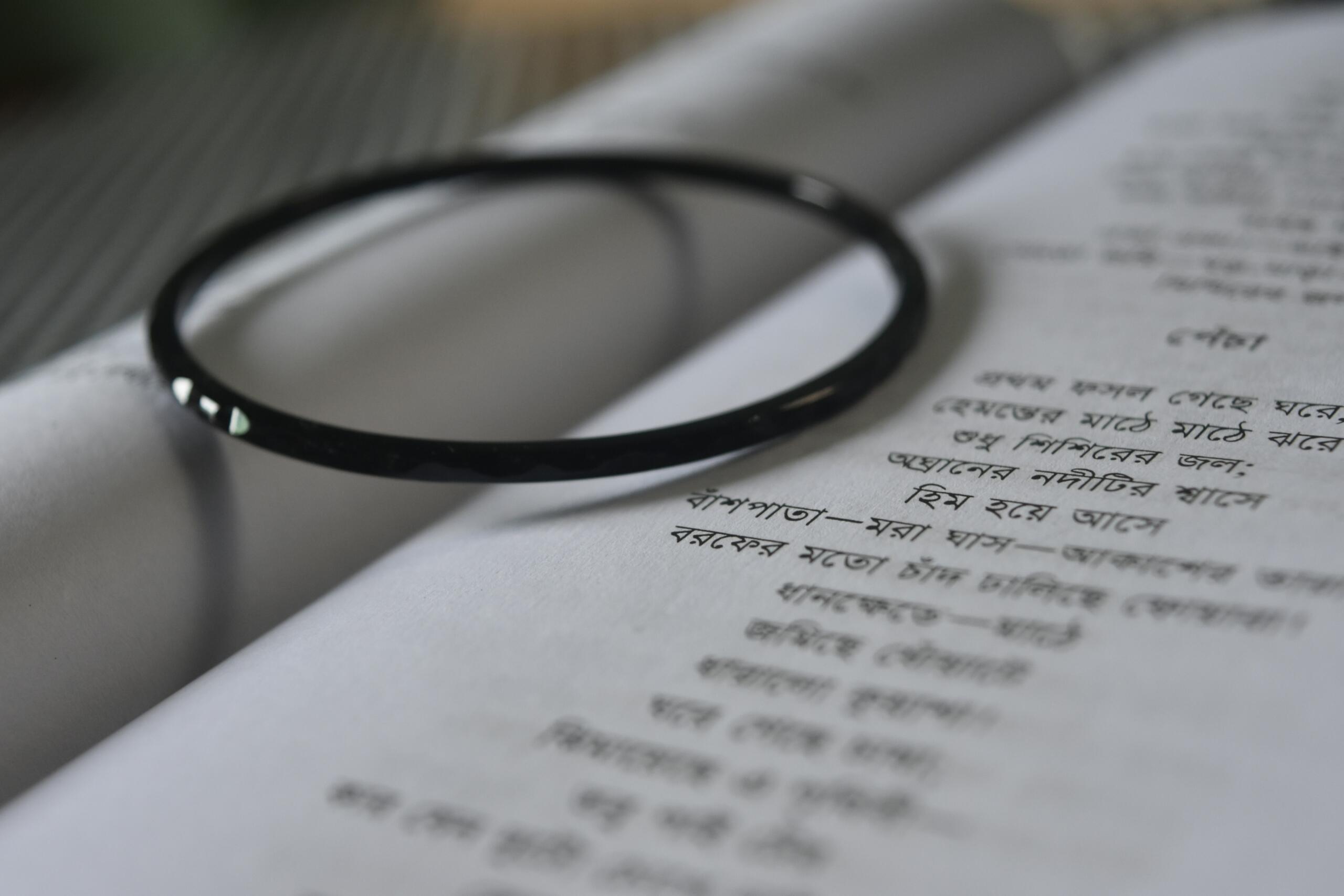 A close-up of a Bengali poetry book with handwritten-style printed Bengali script, with a black bangle resting on the open pages. Ideal for illustrating articles on Bengali language, culture, and greetings.