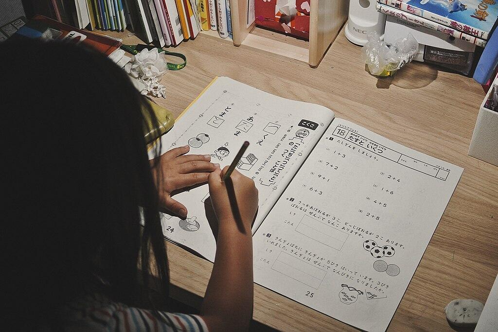 Fëmijë duke bërë detyrat e pushimeve verore në tavolinë, me fletore dhe laps.