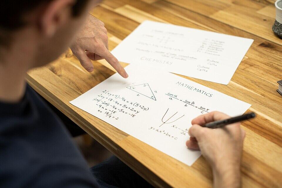 Dorë e tutorit duke treguar ushtrimin e matematikës në fletë.