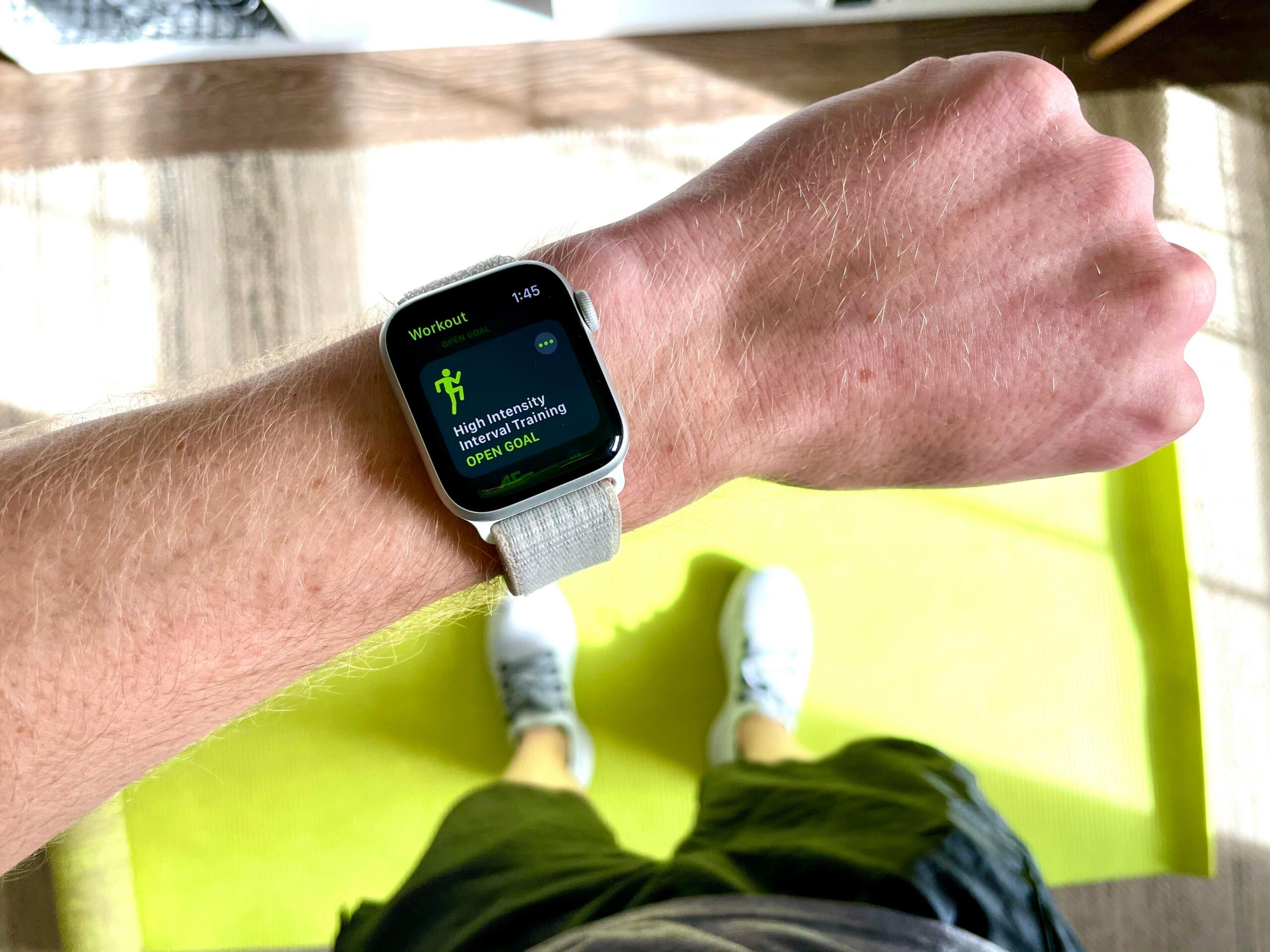 Apple Watch me rrip të bardhë sportiv në kyç — teknologjia e fitnesit si “trajner i dytë” në dorë.