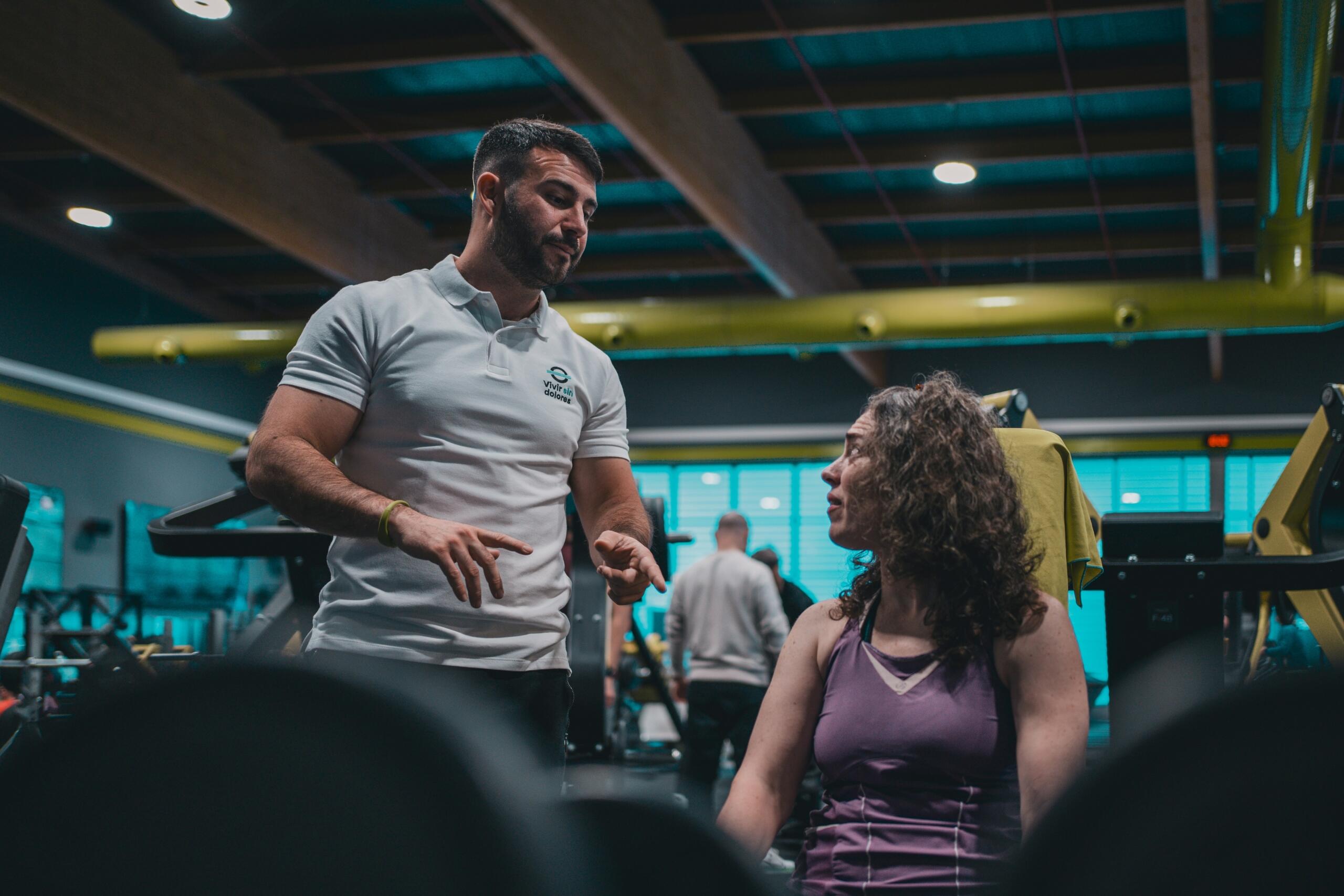 Personal trainer talking to Woman sitting on a gym equipment