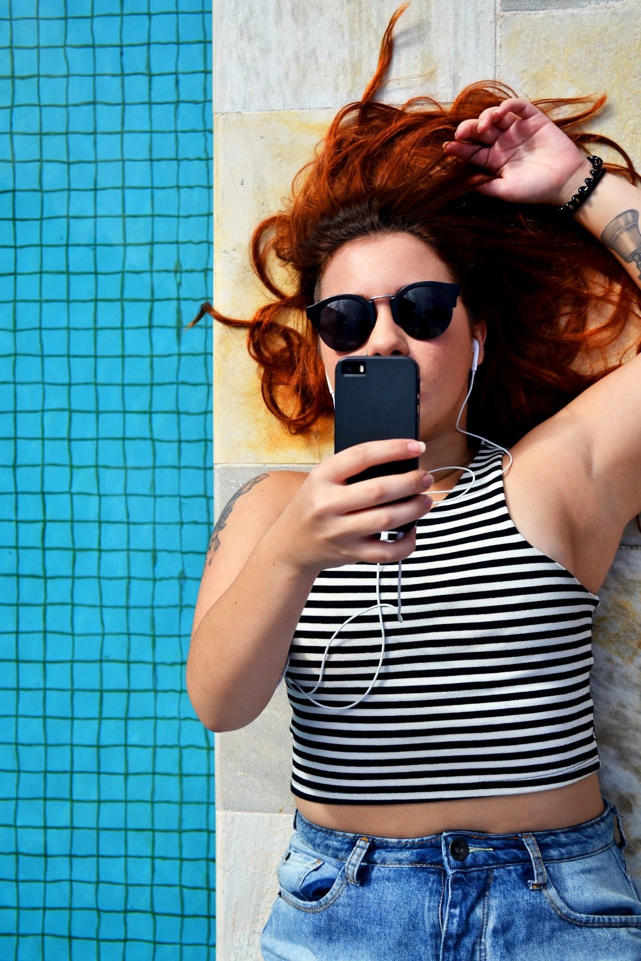 Chica acostada al borde de la pileta usando el celular.