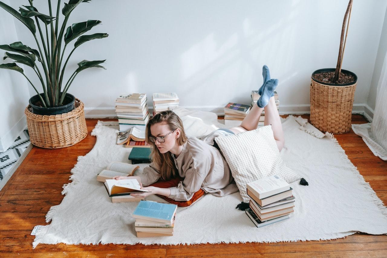 Mujer acostada en el piso rodeada de libros, leyendo