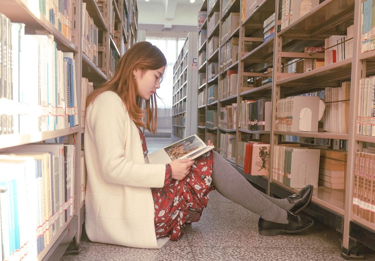 Mujer sentada en el piso de una biblioteca leyendo