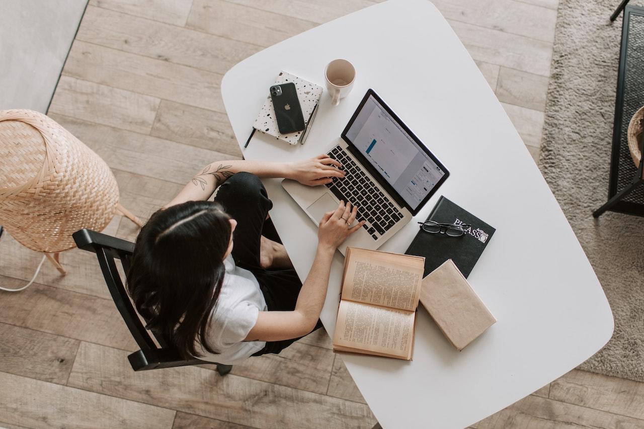 Mujer con su computadora y libros al rededor 