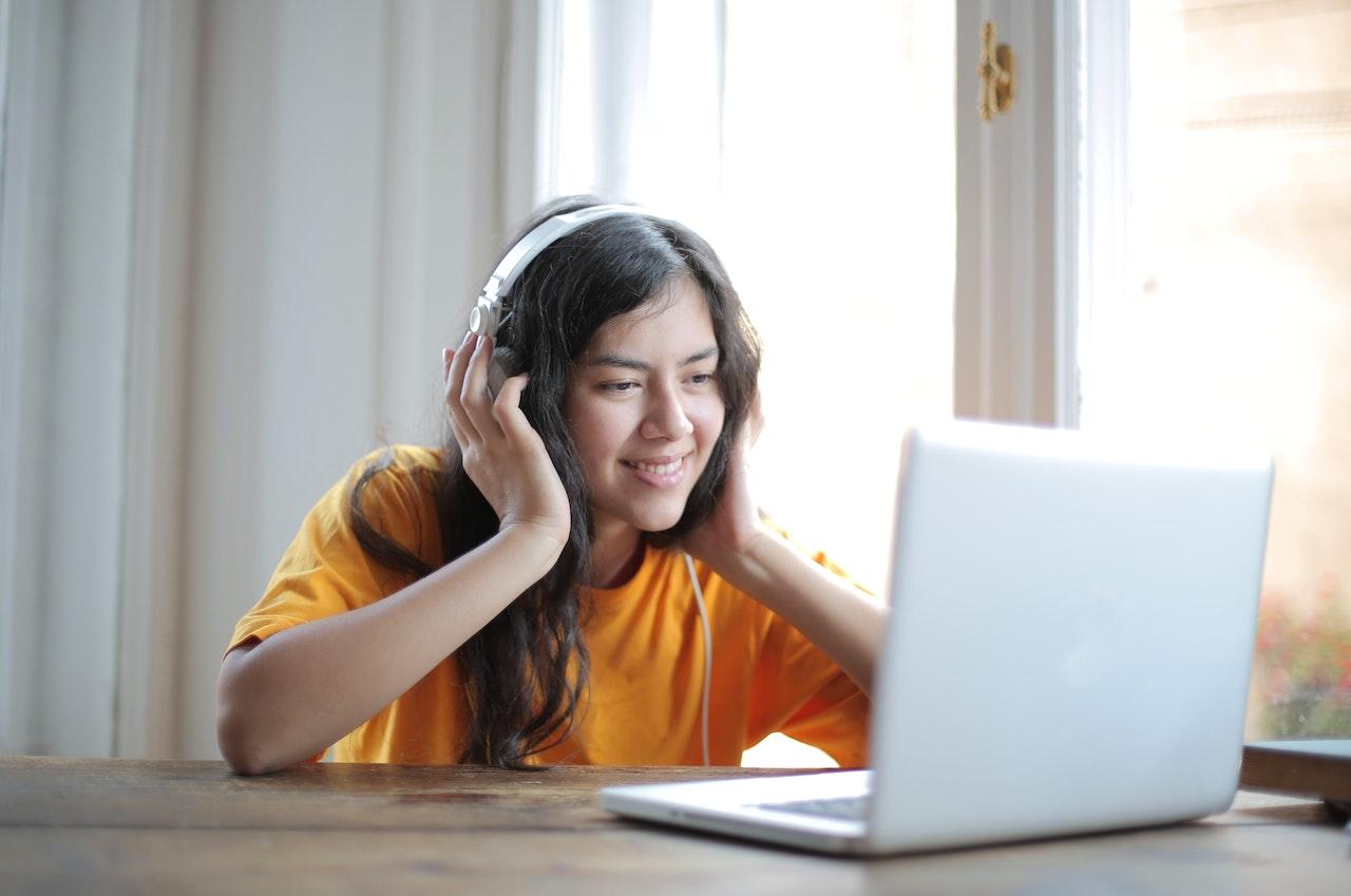 Joven sentada en la mesa con computadora y auriculares.