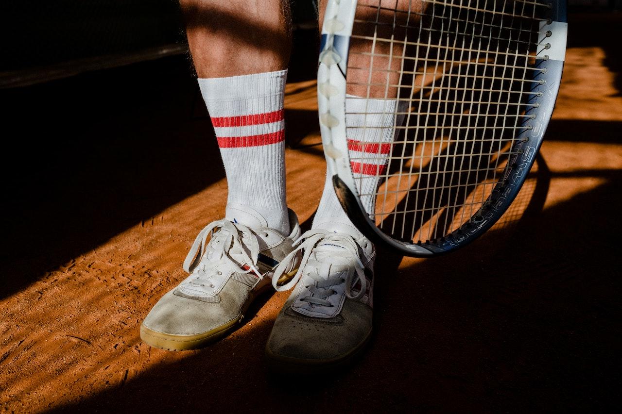 Deportista con zapatillas y raqueta sobre una cancha de tenis. 