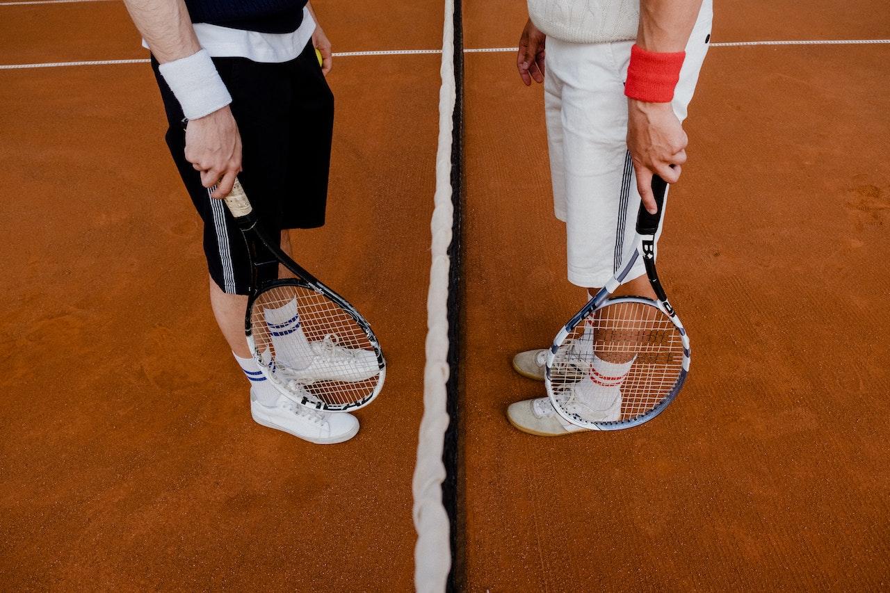 Jugadores parados sobre la cancha de tenis con raquetas en la mano y equipamiento deportivo.