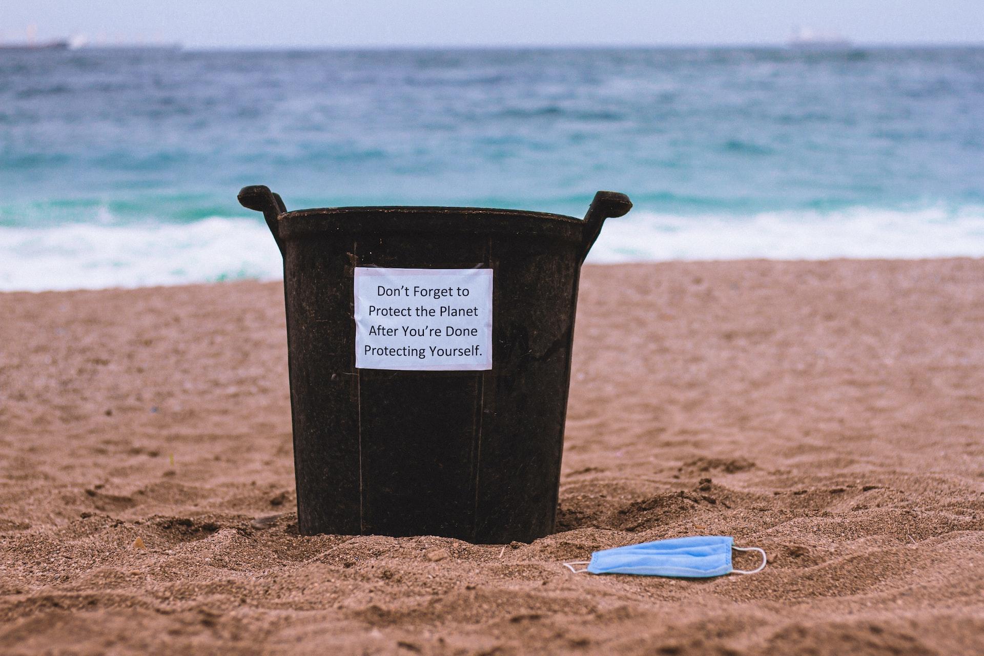 Basurero en la playa con un cartel insinuando que cuidemos nuestro planeta.