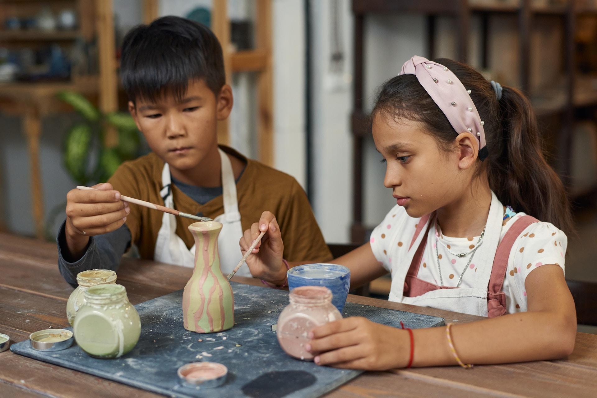 Dos niños pintando una pieza de cerámica.