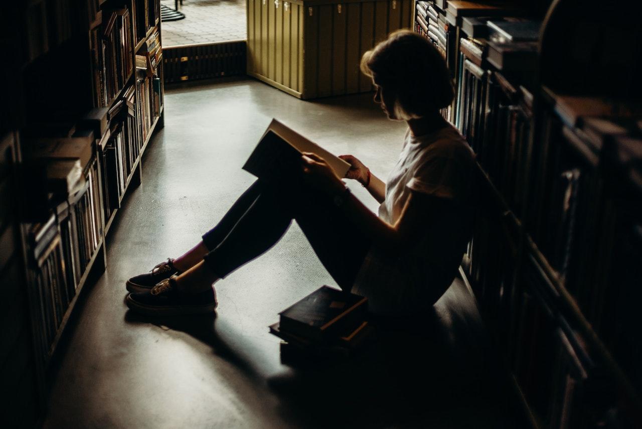 Mujer leyendo sentada en el piso de una biblioteca.