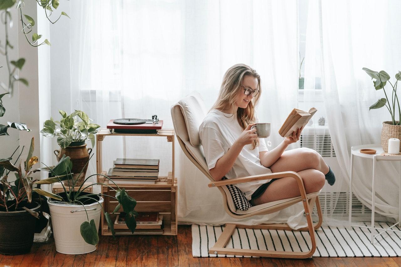 Chica leyendo en el sillón con una taza de café.