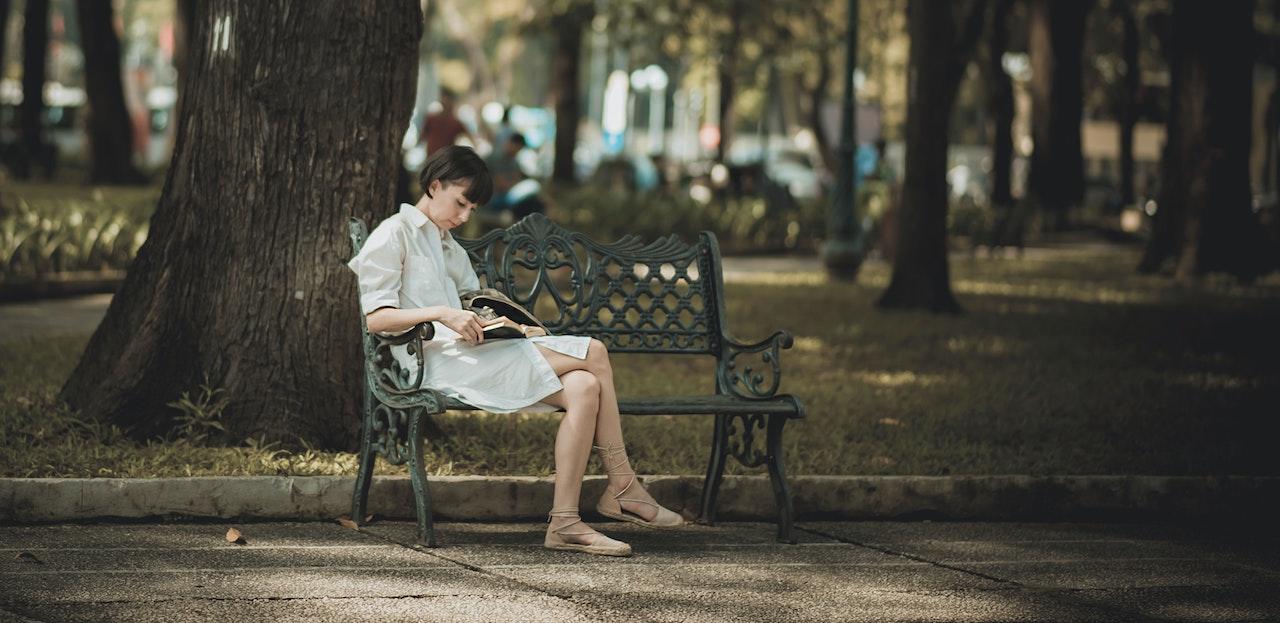 Mujer leyendo en un banco de plaza.