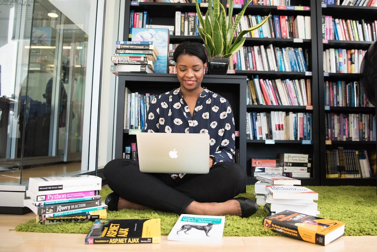 Mujer sentada en el suelo con computadora y libros a su alrededor.