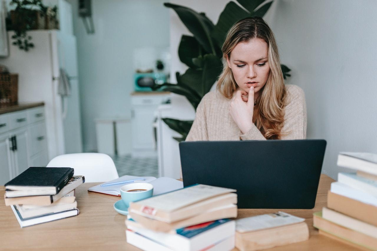 Mujer trabajando en la computadora con libros sobre la mesa. 