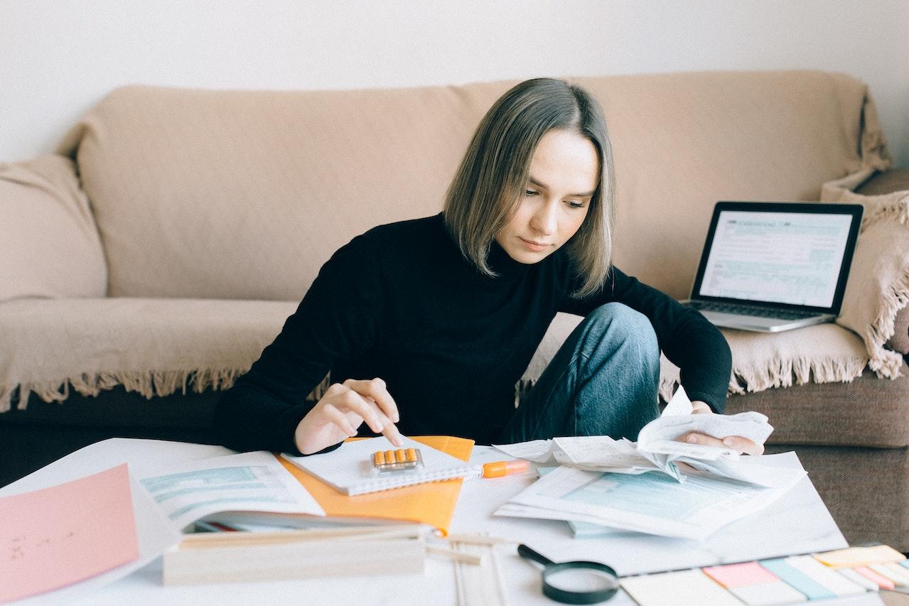 Mujer con calculadora, papeles sobre la mesa, y computadora abierta en el sillón.