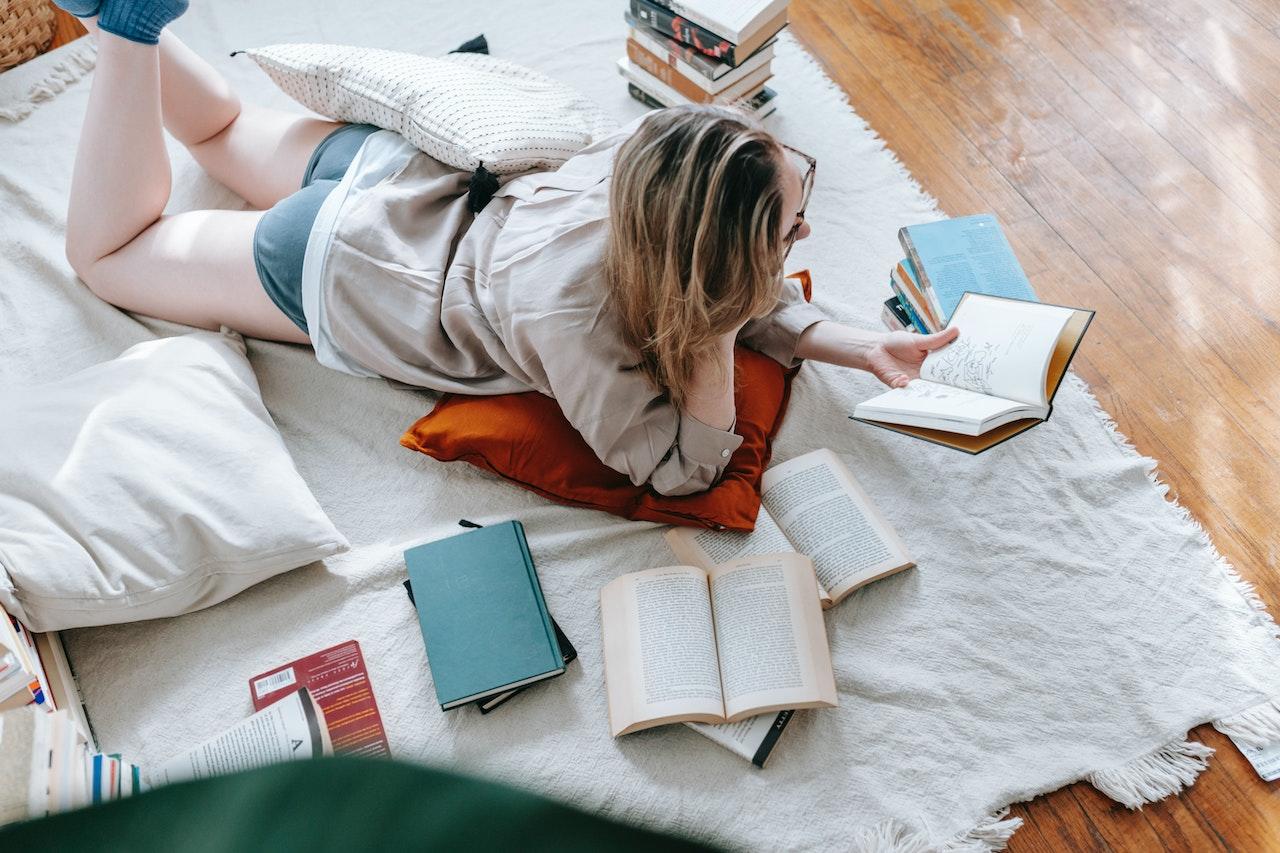 Chica acostada junto a mucho libros, leyendo