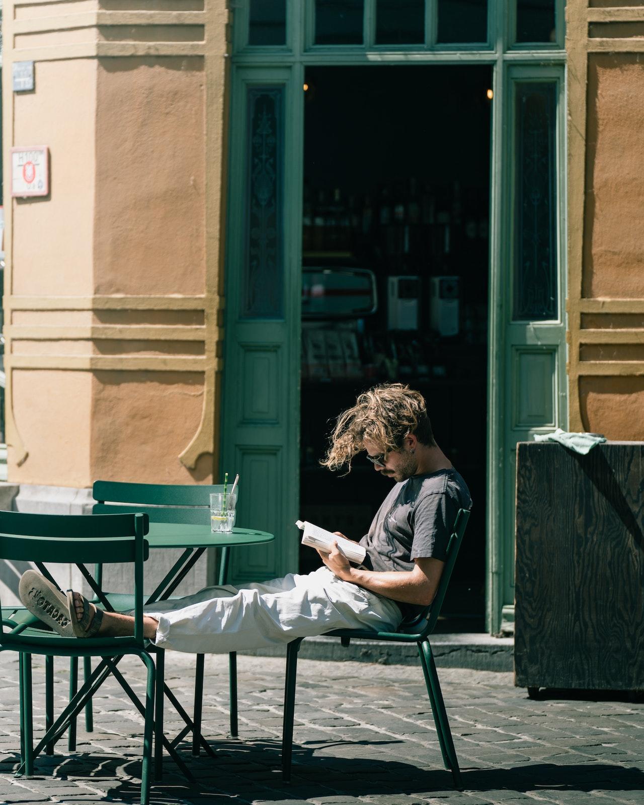 Hombre leyendo en una mesa sobre la vereda.