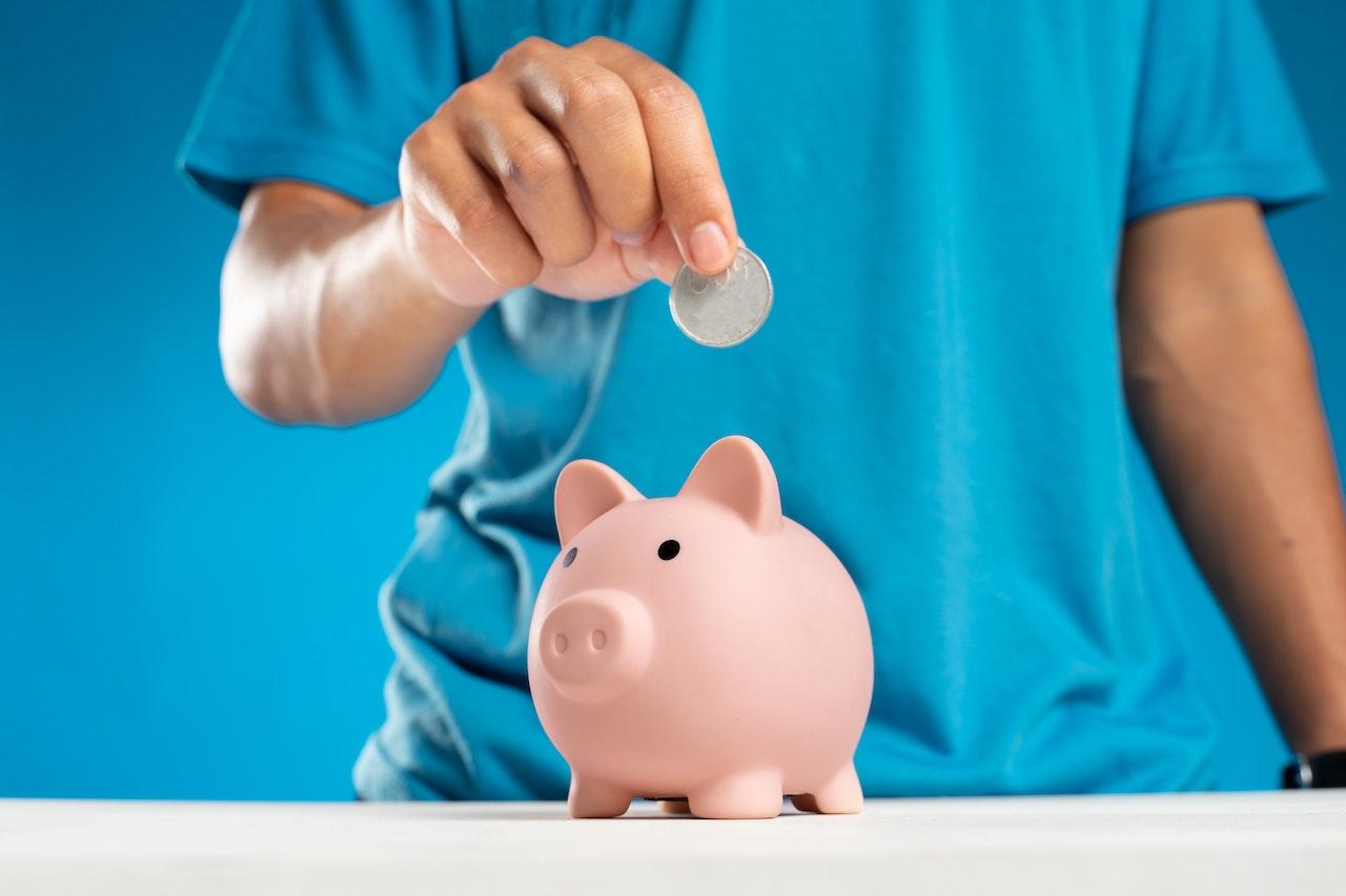 Persona introduciendo una moneda en una alcancía con forma de cerdito.