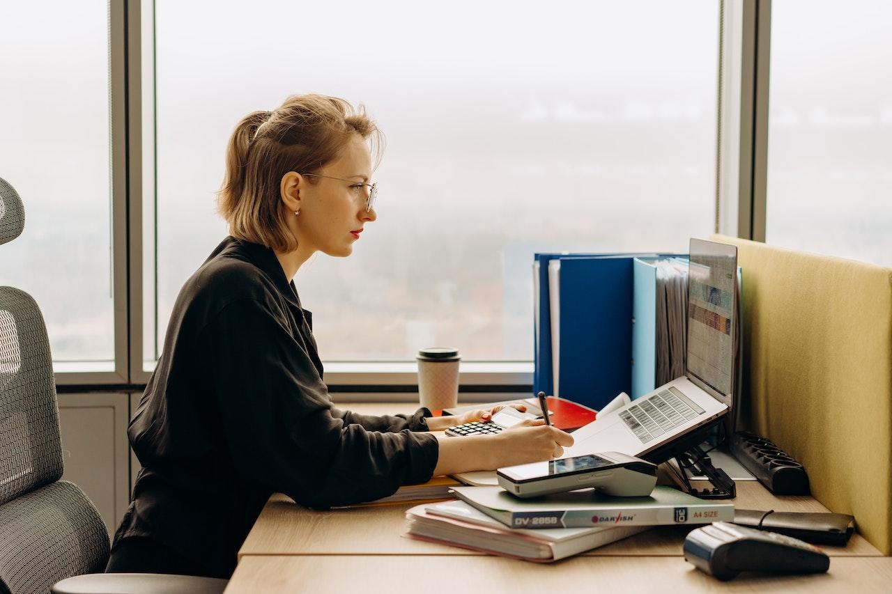 Mujer sentada frente a la computadora con calculadora y posnet.