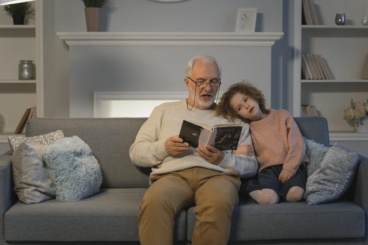 Abuelo y nieta leyendo un libro, sentados en el sillón.