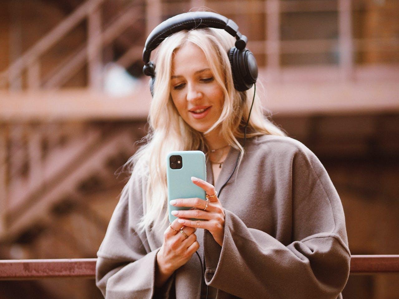 Mujer con auriculares y celular en la mano.