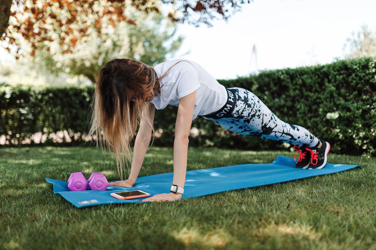 Mujer haciendo flexiones en un mat sobre el césped. 