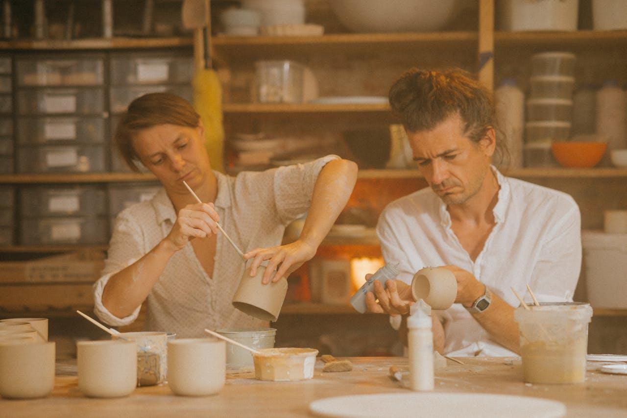 Dos personas sentadas pintando objetos de cerámica.