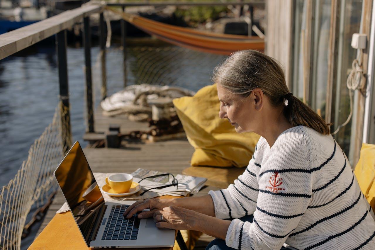 Mujer sentada en un muelles con la computadora sobre la mesa