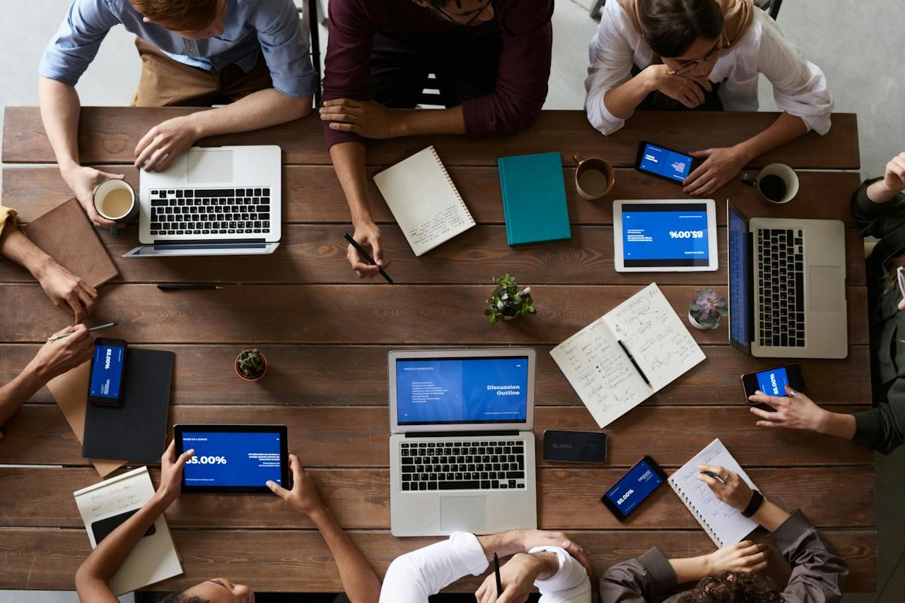 Brazos de personas y computadoras sobre una mesa.