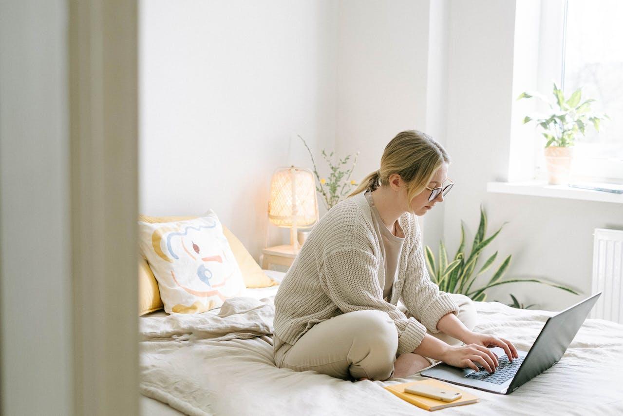 Mujer sentada en la cama con tipeando en la computadora. 