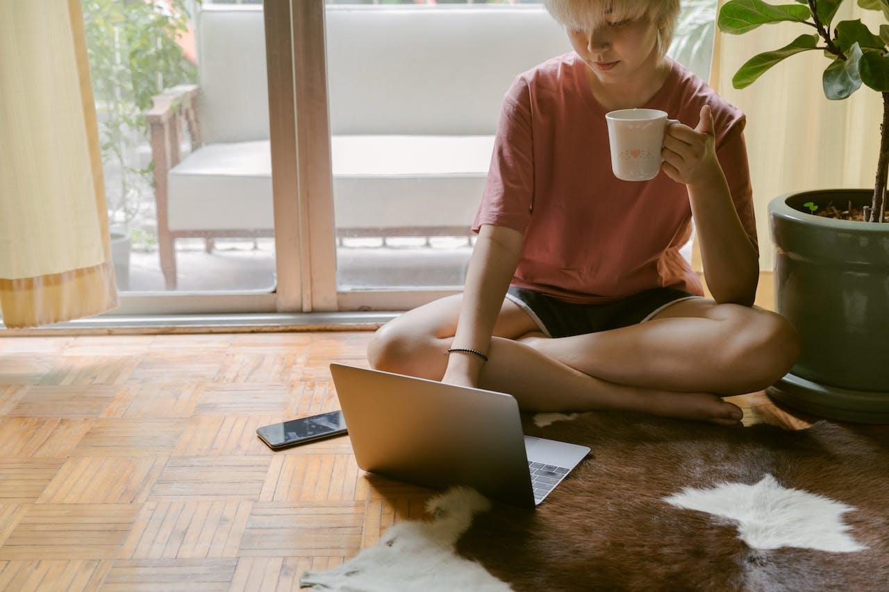 Mujer sentada en el suelo con una computadora y un café.
