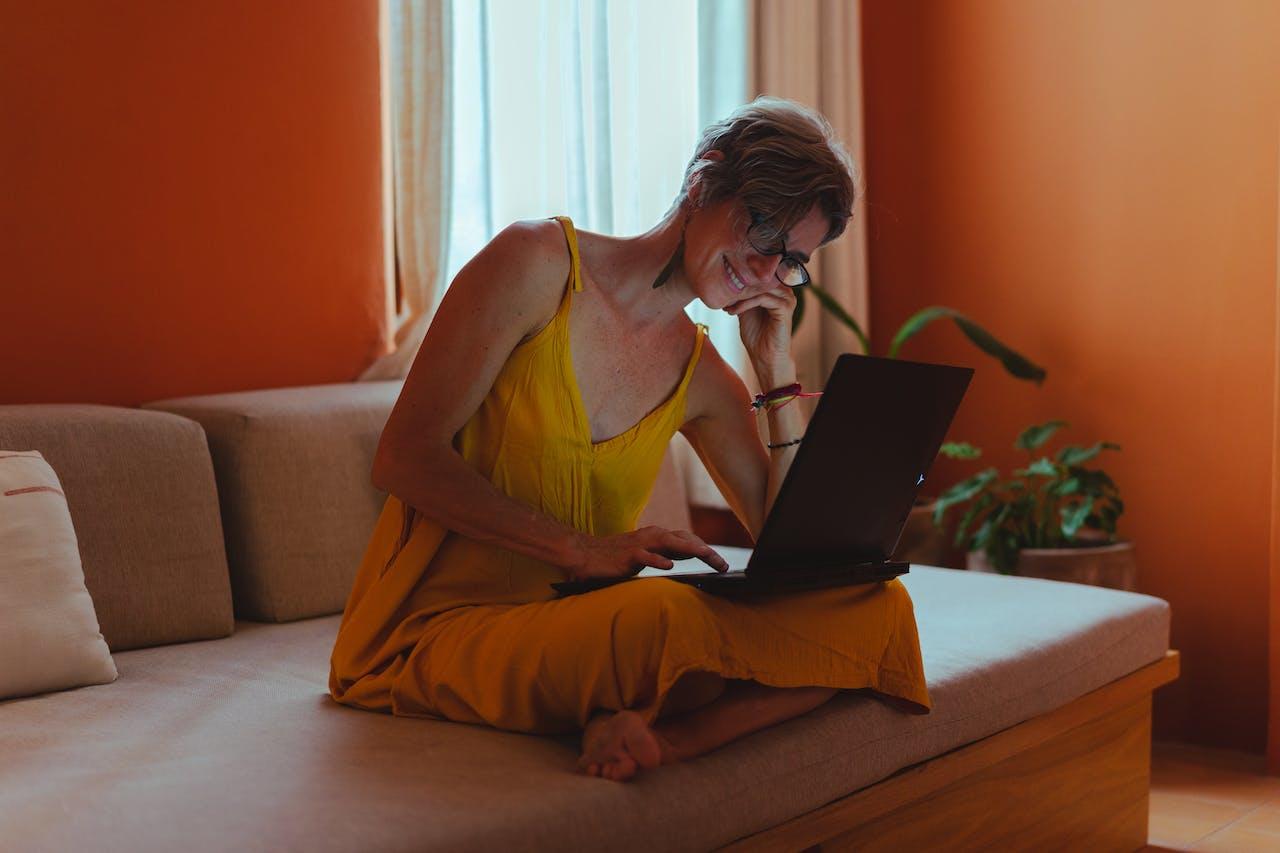 Mujer sentada en els illon con la computadora sobre sus piernas. 