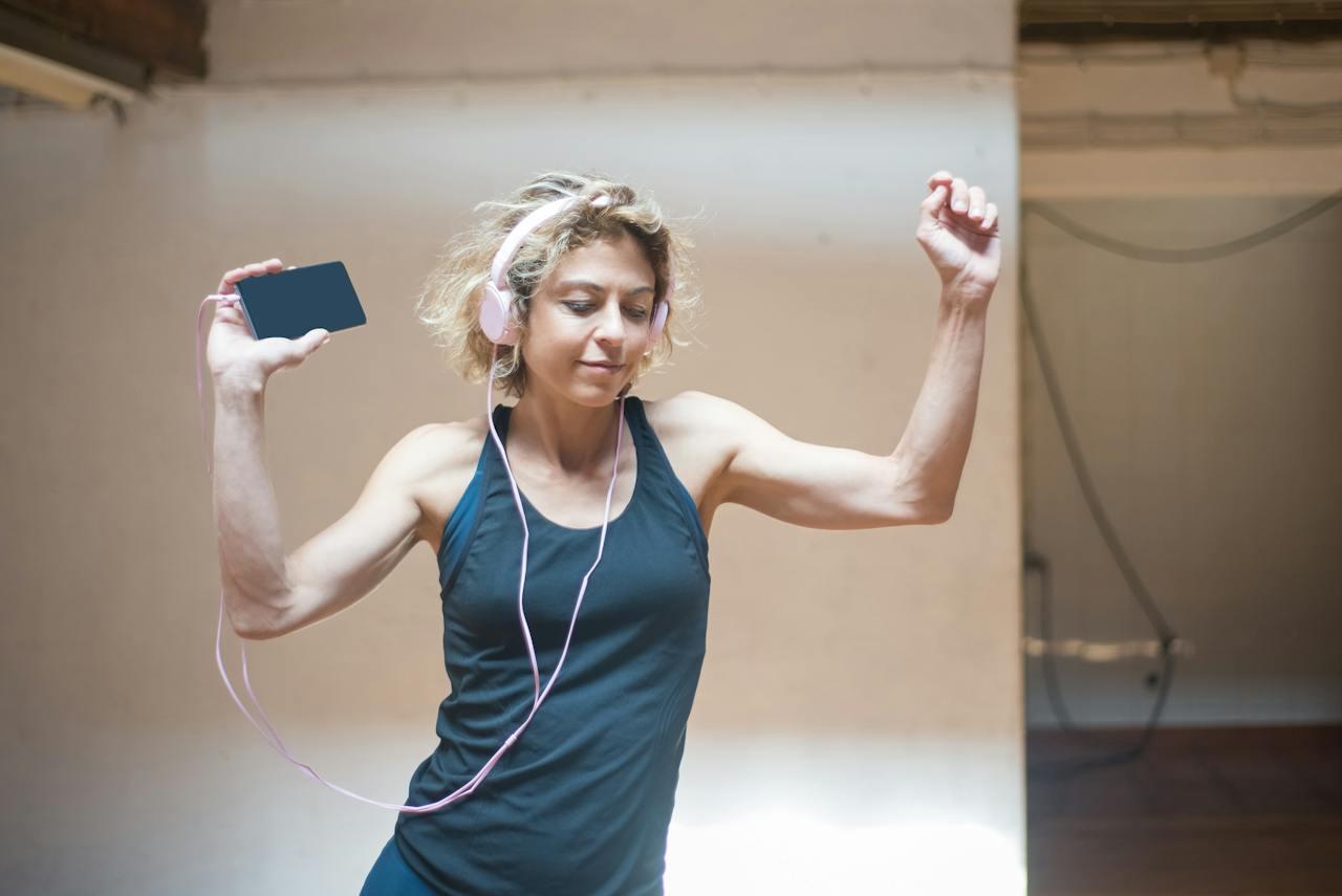 Mujer bailando con auriculares y celular en la mano.