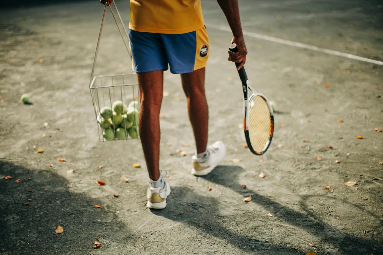Persona caminando con pelotas y raquetas de tenis.