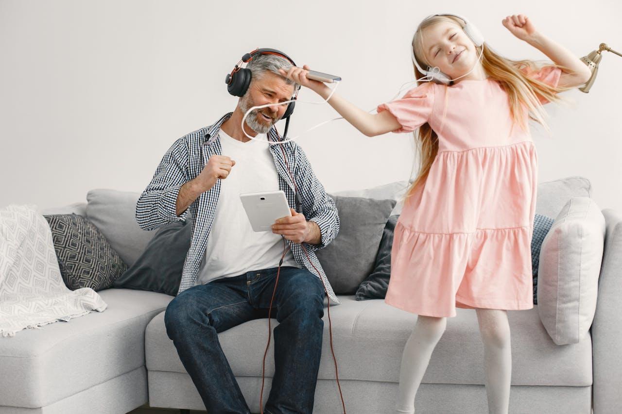 Adulto sentado y niña con vestido rosa bailando con auriculares.
