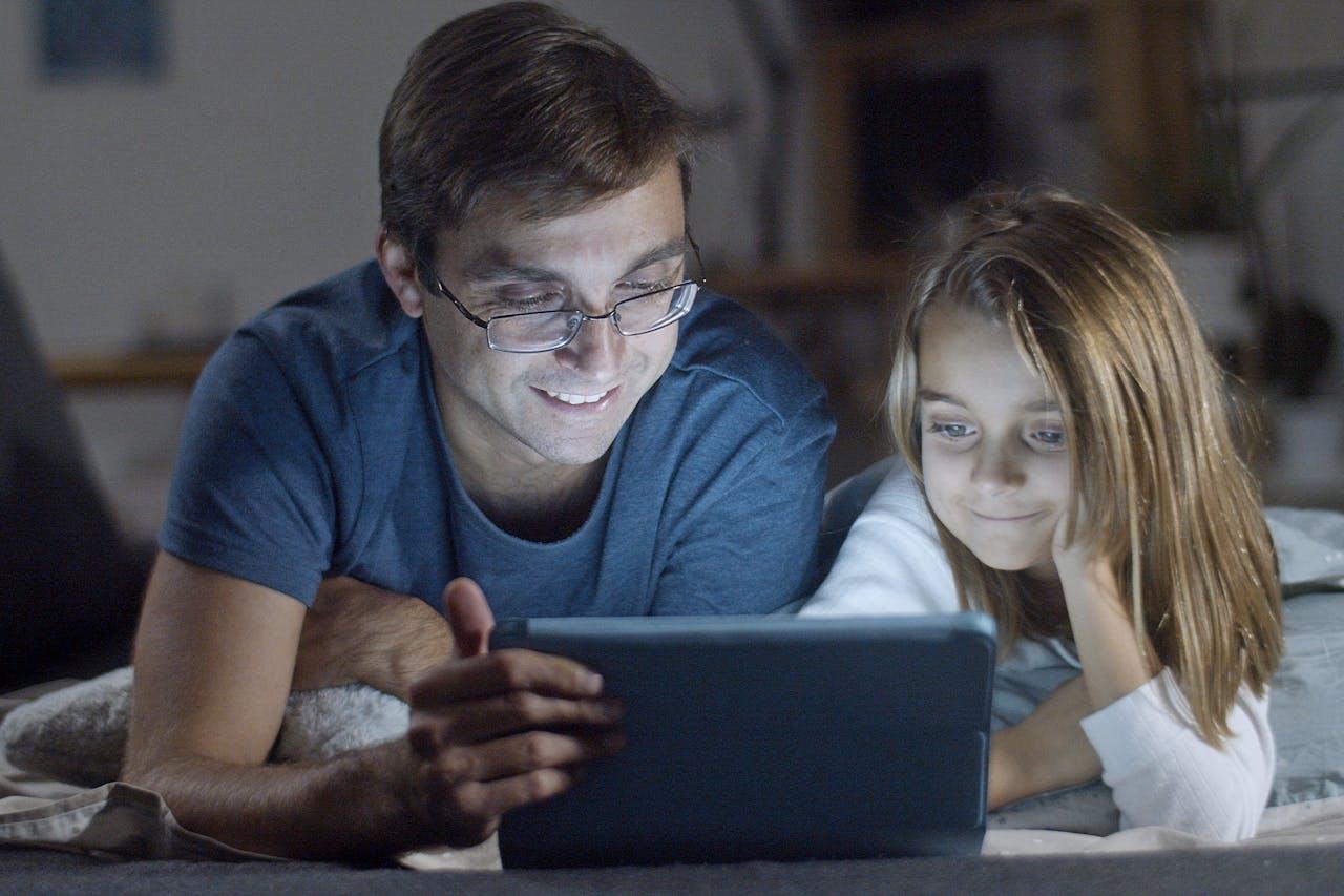 Niña y adulto, recostados mirando una tablet.