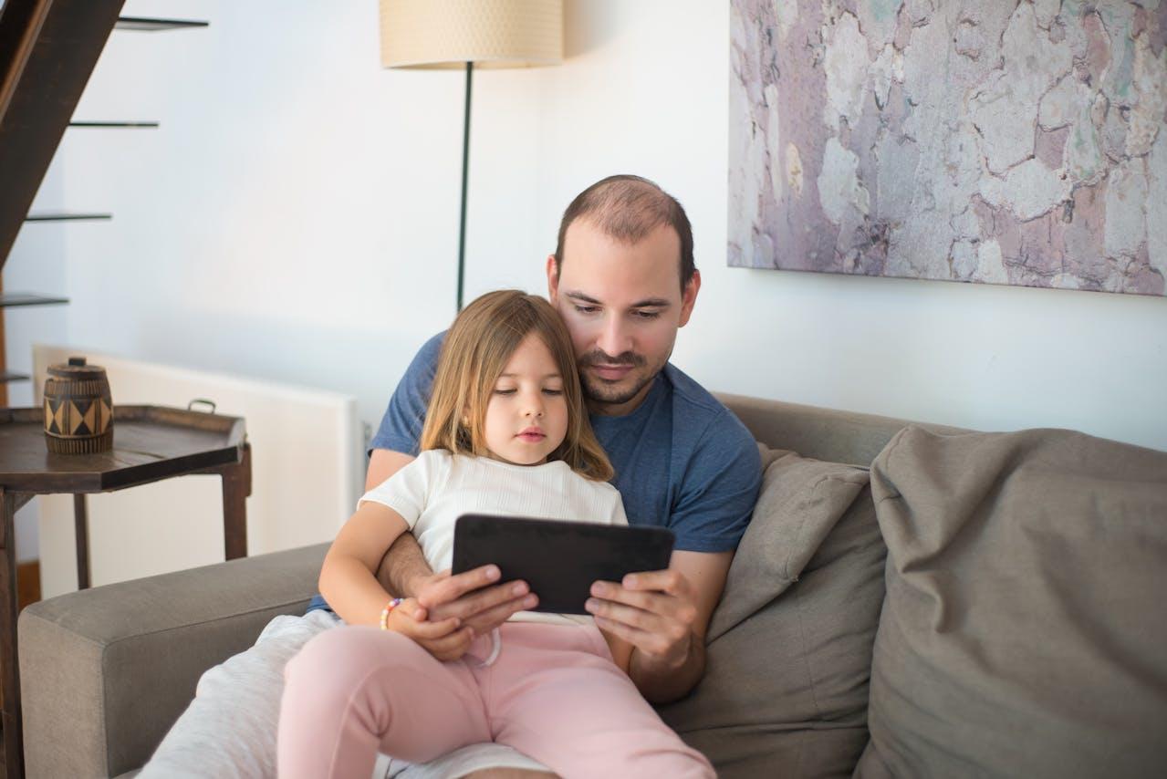 Adulto y niña mirando la tablet sentados en el sillón.