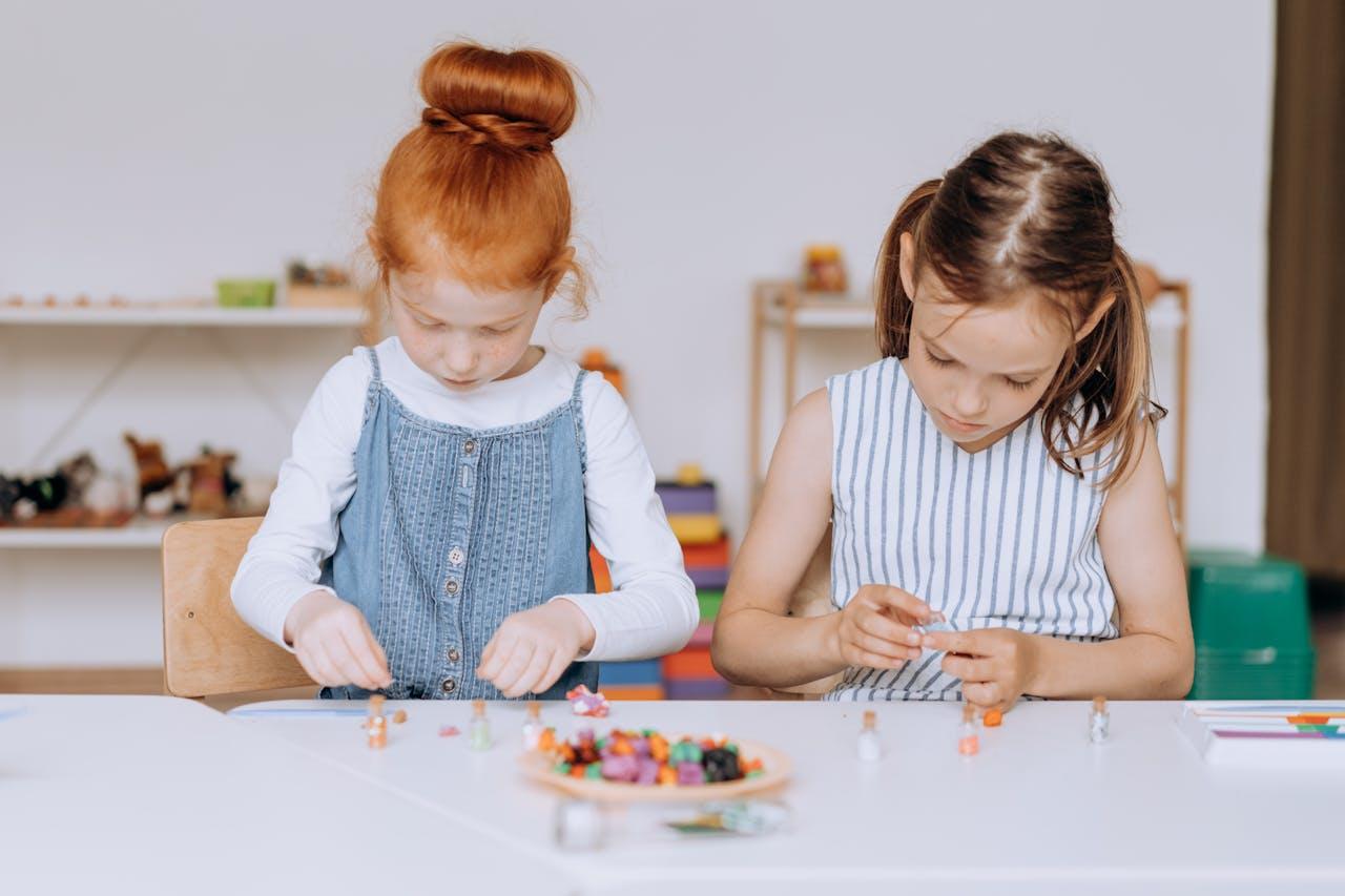 Dos niñas haciendo collares sobre la mesa.