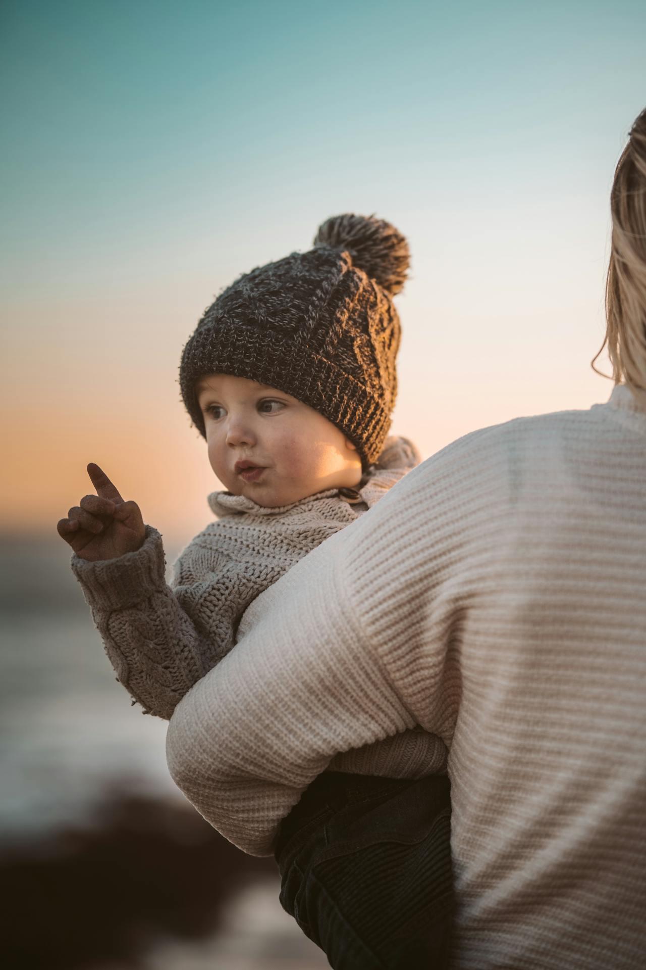 Bebé con gorro marrón y cielo de fondo.