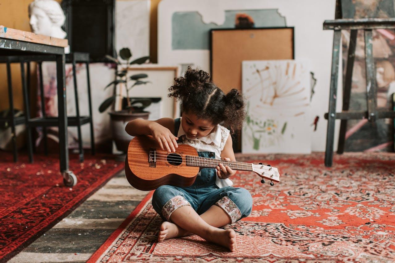 Niña sentada en la alfombra tocando la guitarra.