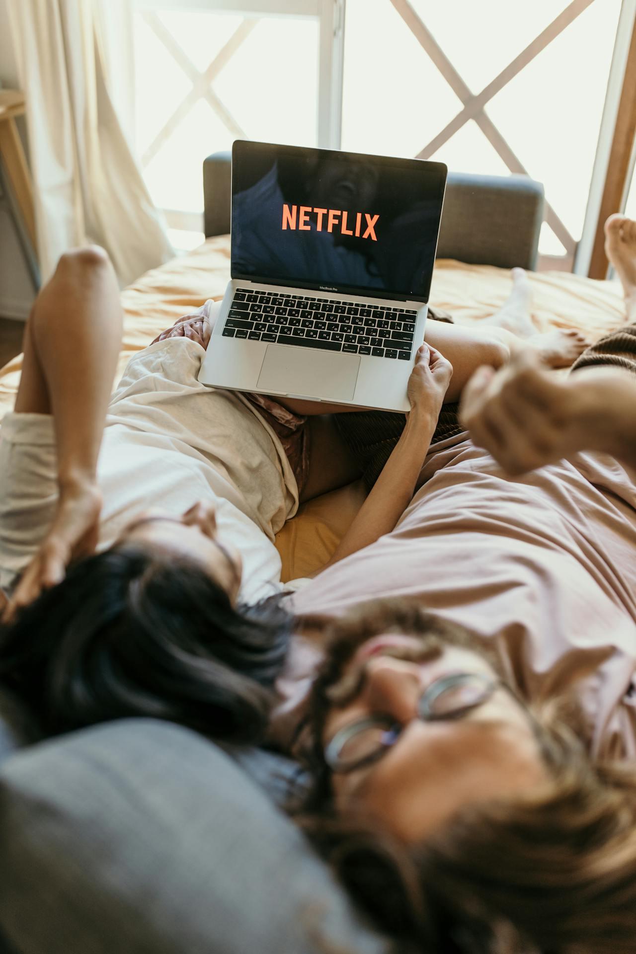 Dos personas acostadas en la cama viendo Netflix en la computadora.