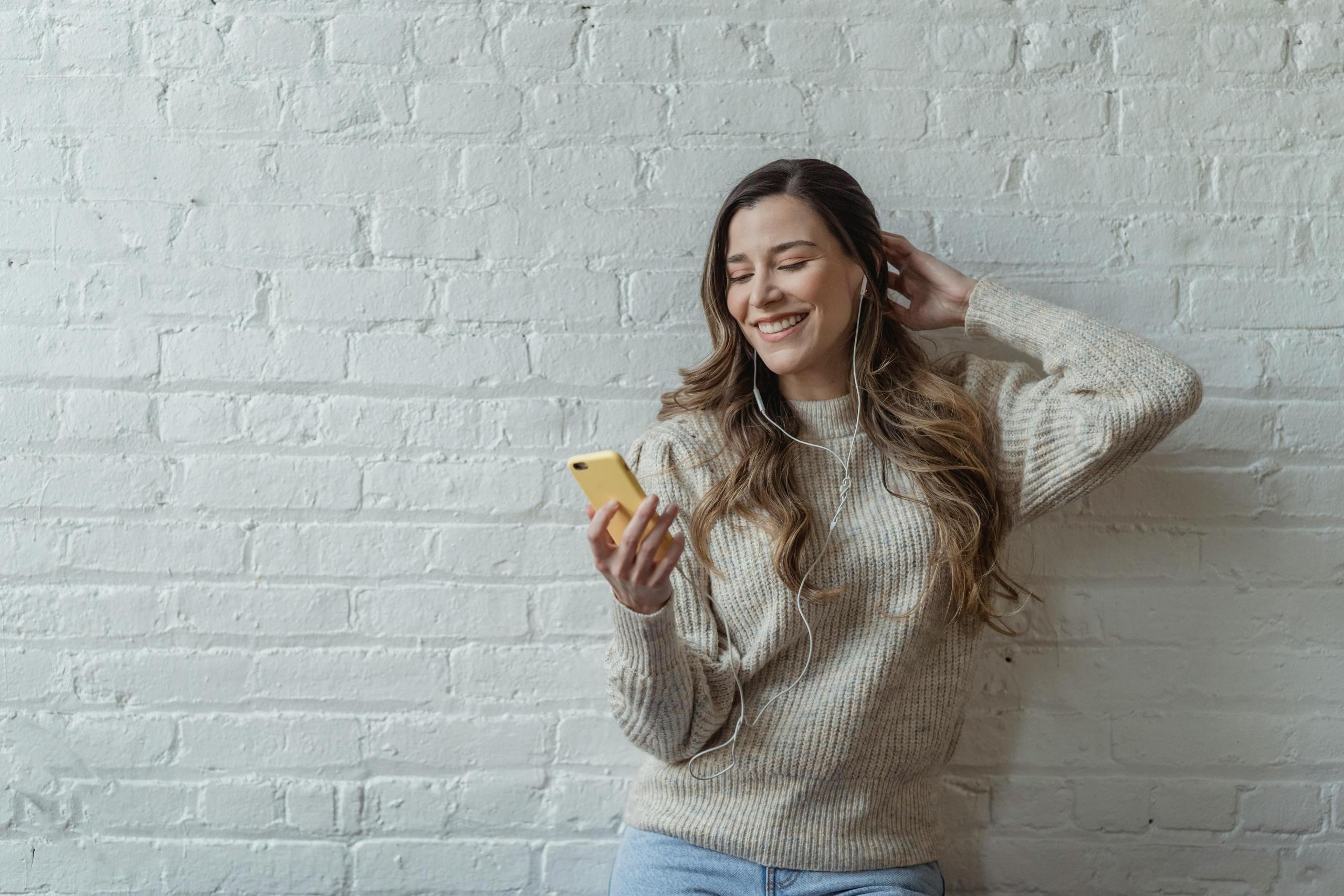 Mujer sonriendo con auriculares y celular.