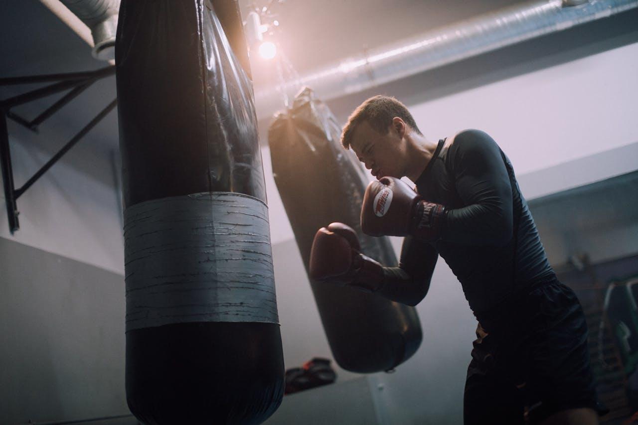 Hombre cuan guantes de box vestido de negro frente a la bolsa de boxeo.