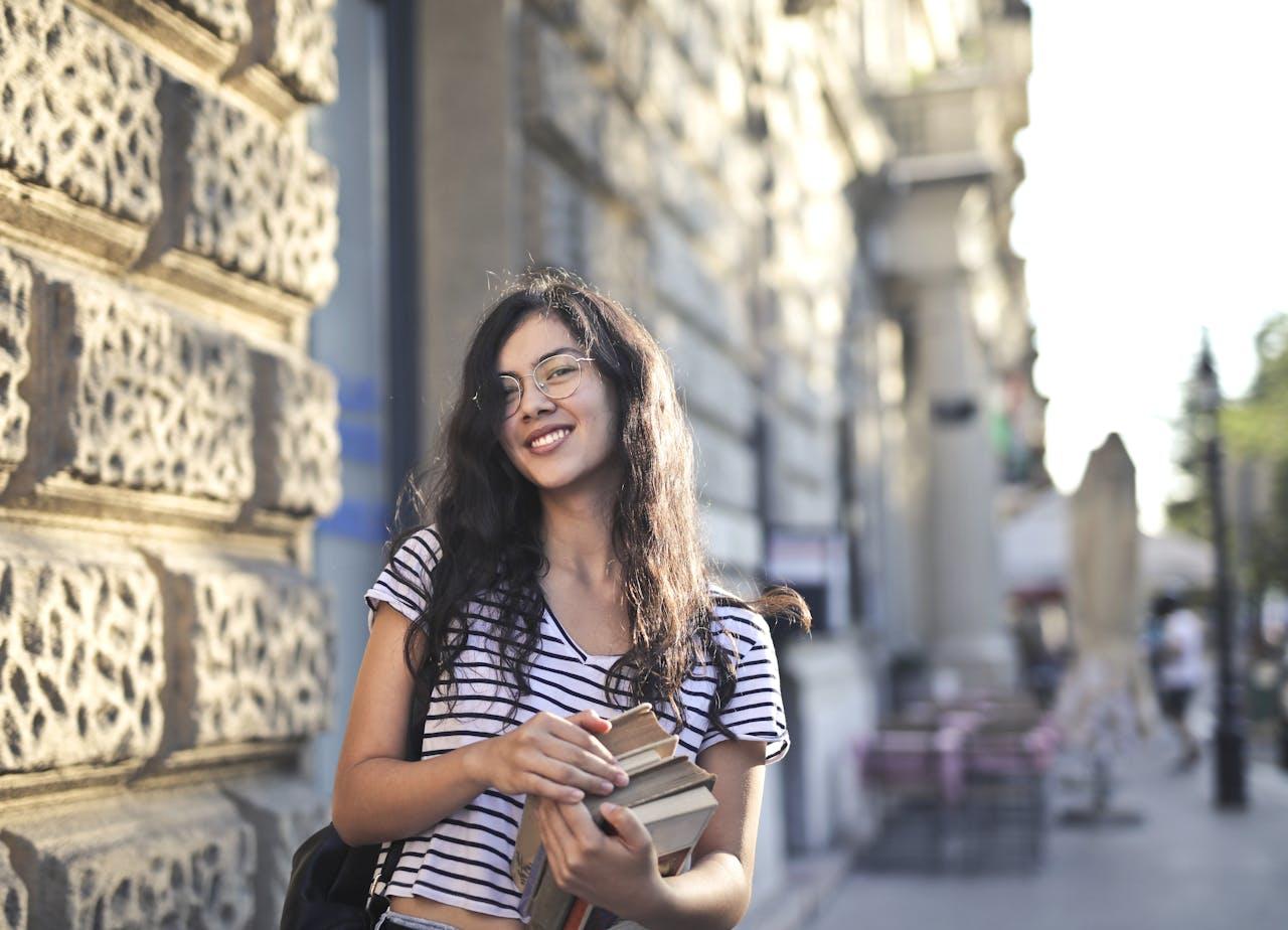 Mujer jóven con libros en sus brazos.