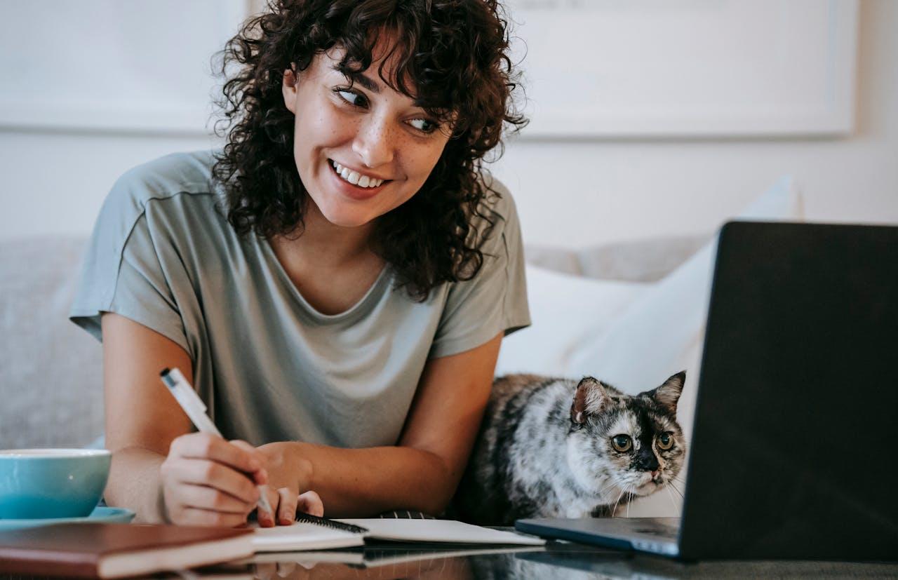 Mujer con remera gris y gato negro y marrón frente al ordenador.