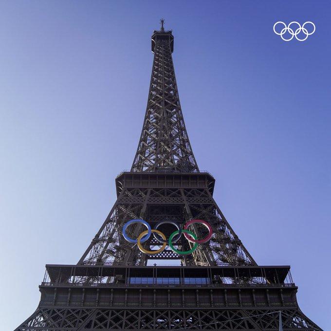 Torre Eiffel con aros de colores sobre fondo de cielo celeste.