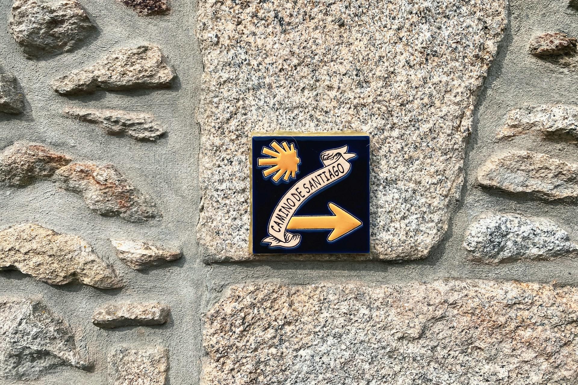 Azulejo azul con flecha amarilla sobre pared de piedra.